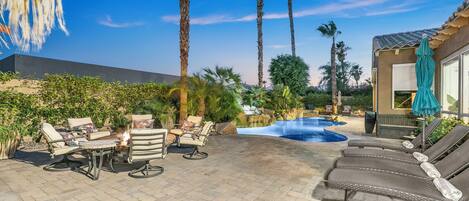 A patio with lounge chairs, a fire pit, and a swimming pool.
