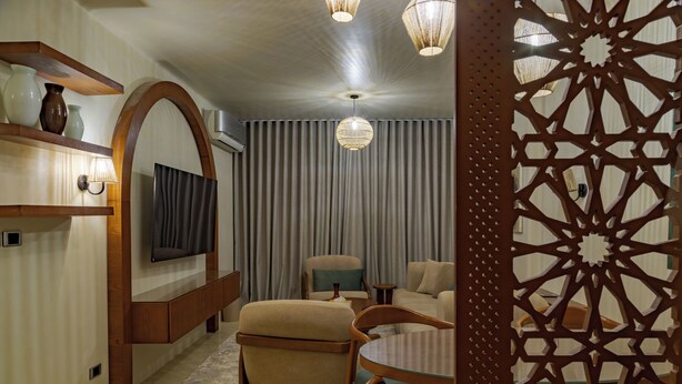 A modern living room with a flat-screen TV, a sofa, a coffee table, and a decorative wooden partition. - Minimal Mediterranean Apt. (New Cairo)