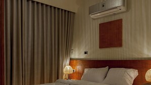 A well-lit bedroom with a large bed, an air conditioning unit, a wooden headboard, and a hanging light fixture. - Minimal Mediterranean Apt. (New Cairo)