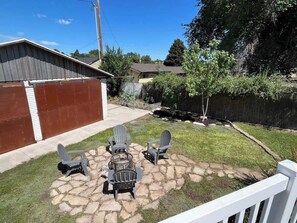 A backyard with a stone fire pit and four Adirondack chairs arranged around it.