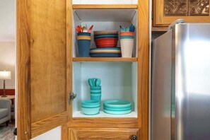 A wooden cabinet with a stainless steel refrigerator, containing stacked plates and bowls.