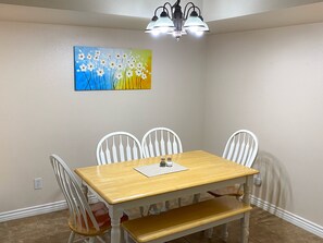 Un comedor con mesa de madera, sillas blancas, un banco y un cuadro en la pared.