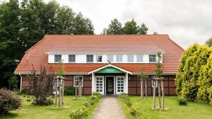 A two-story building with a red-tiled roof and a green entrance sign. - Seehotel Köllnitz (Storkow)