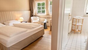 A hotel room with a bed, a chair, a small table, and a window with curtains. - Seehotel Köllnitz (Storkow)