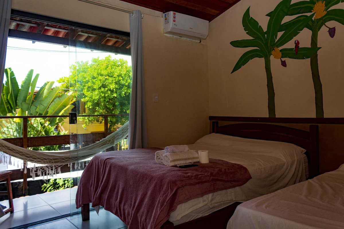 Quarto com cama, rede e vista para o verde lá fora.