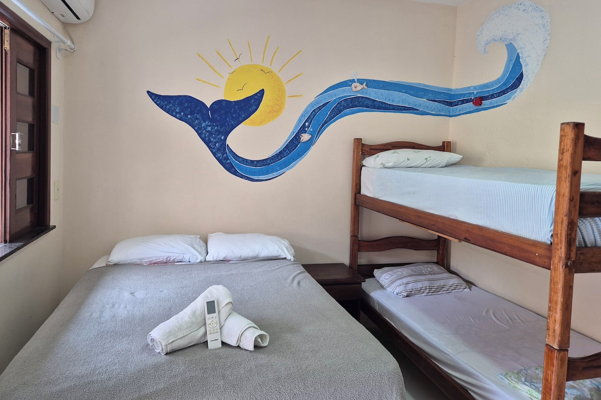 Quarto com beliches, uma toalha no beliche inferior e um mural na parede com um golfinho e sol.
