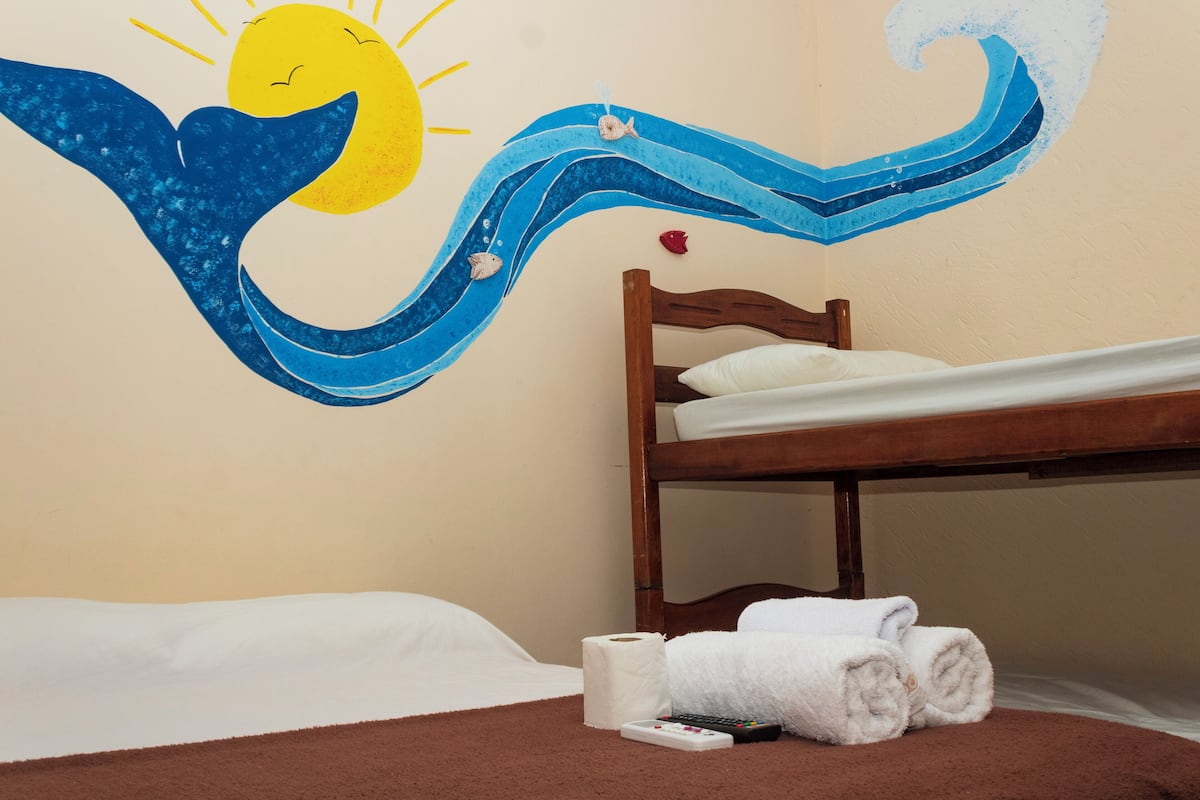 Quarto com beliche, painel decorativo de sol e ondas, rolo de papel higiénico e comando remoto.