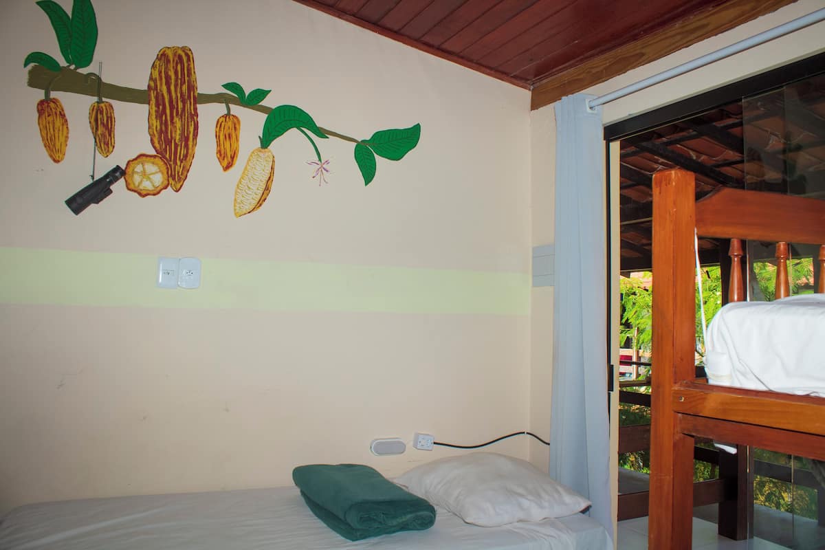Uma cama de solteiro com uma toalha verde, um travesseiro branco e um mural na parede com vagens de cacau.