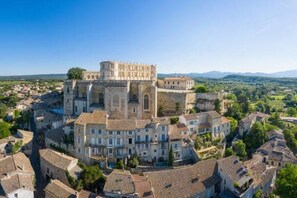 A historic building with a fortified structure, surrounded by traditional buildings and a view of the countryside.