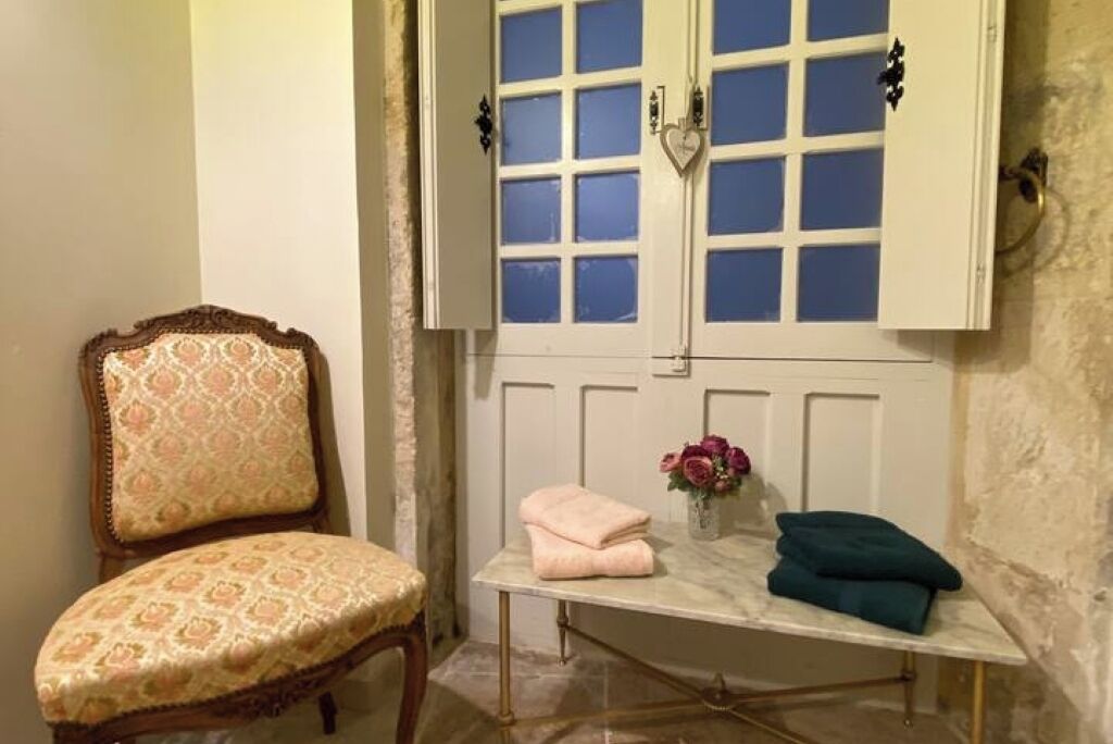A room with a vintage chair, a marble table with folded towels, and a window with a heart-shaped decoration.