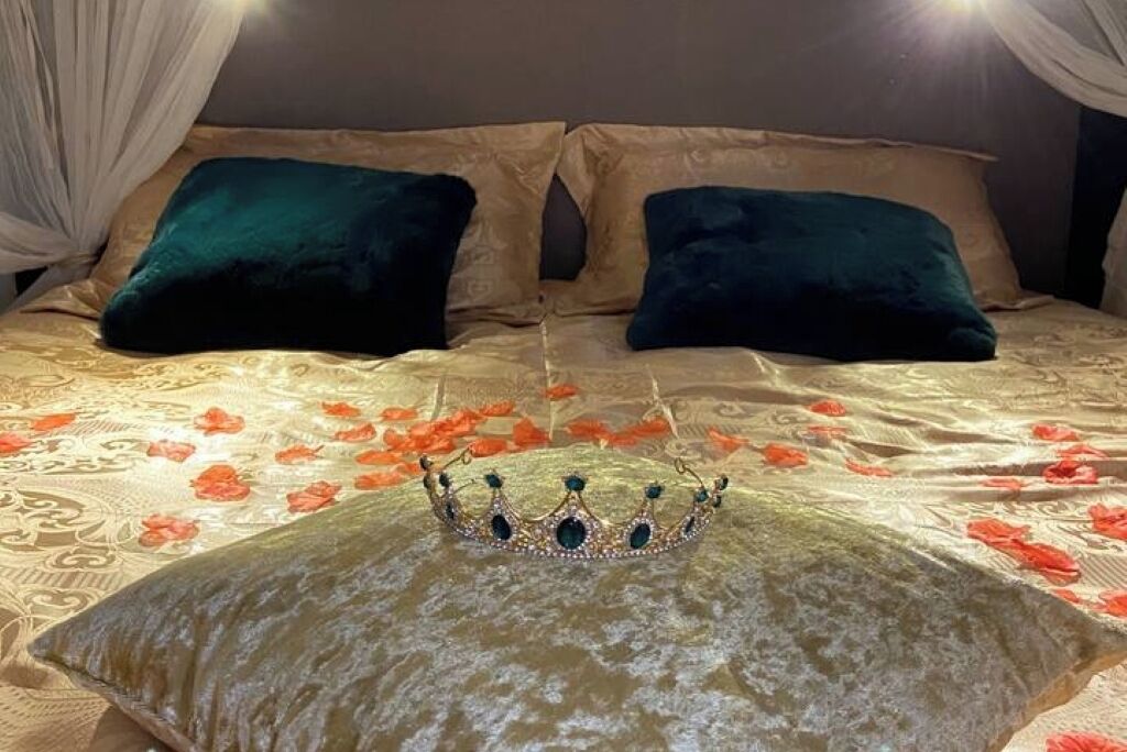 Ein Bett mit einer blumigen Tagesdecke, zwei dunkelgrünen Kissen und einer dekorativen Krone auf einem Kissen.