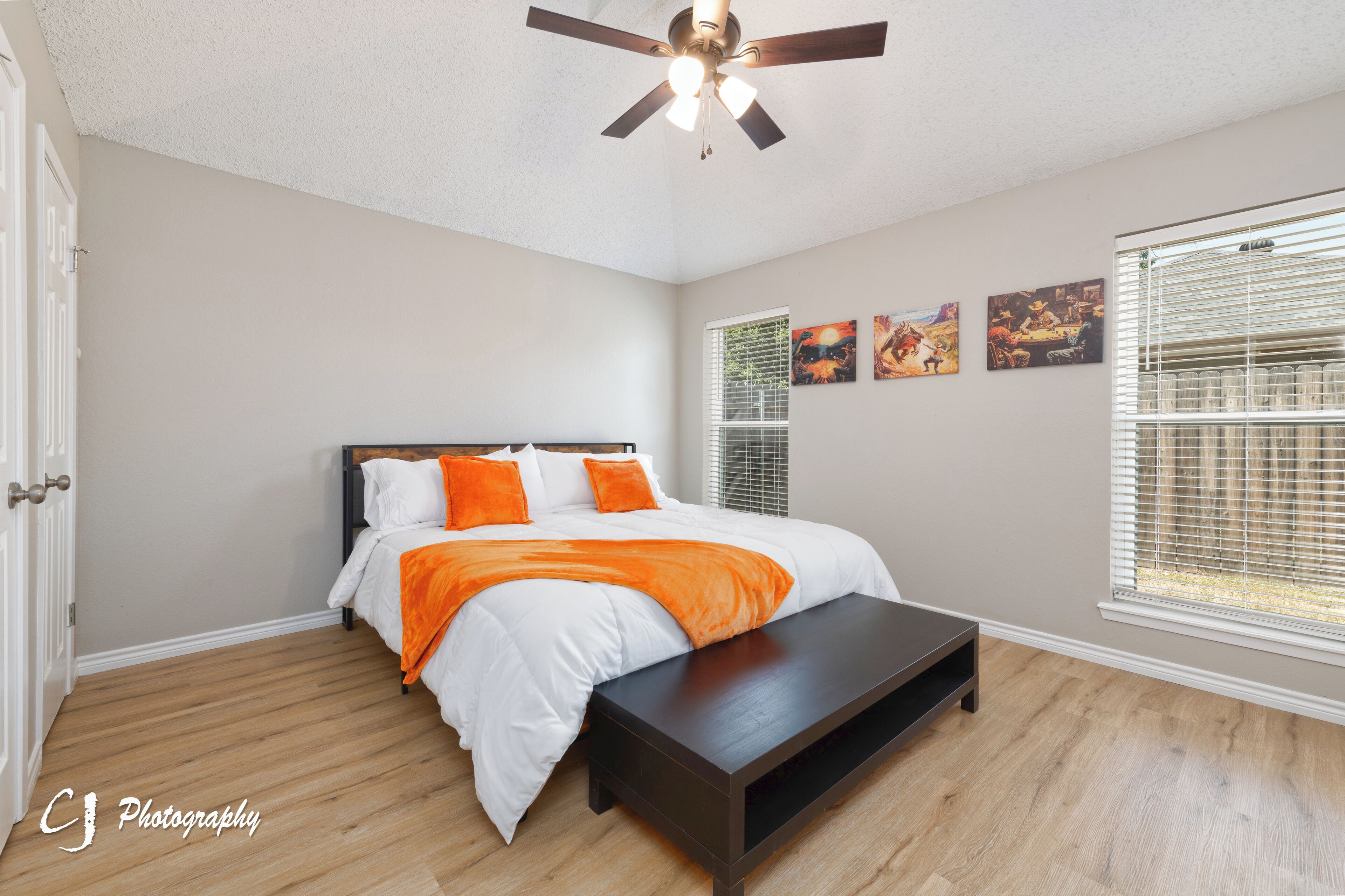 A bedroom with a bed, a bench, a ceiling fan, and artwork on the wall.