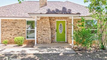 A brick house with a green door, a small porch, and a chimney.