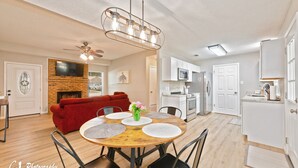 A modern kitchen with white cabinets, a microwave, and a stove. There is a dining area with a wooden table and chairs, and a red sofa in the living room. - Rex Ranch is a comfortable conveniently located 3 bedroom 2 bath home. (Abilene)