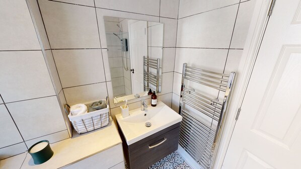 Une salle de bain avec un lavabo blanc, un miroir, un porte-serviettes et une petite poubelle.
