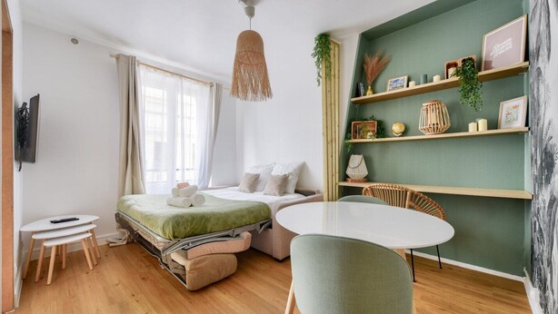 A cozy bedroom with a bed, bedside table, chair, and a small table with a lamp. - Studio Chic & Bohème aux Portes de Paris (Levallois-Perret)