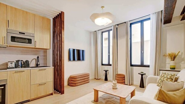 A modern living room with a sofa, a coffee table, and a kitchen area with wooden cabinets and a microwave. - A Sophisticated 2-BR/2BA - Montorgueil (Paris)