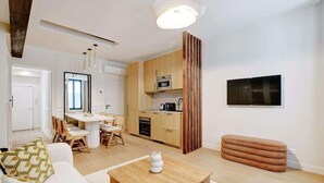A modern living room with a sofa, coffee table, and dining area. A kitchen is visible with wooden cabinets and a microwave. - A Sophisticated 2-BR/2BA - Montorgueil (Paris)