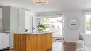 A modern kitchen with a wooden island, white cabinetry, and a large mirror on the wall. - Cove Cottage South West Rocks (South West Rocks)