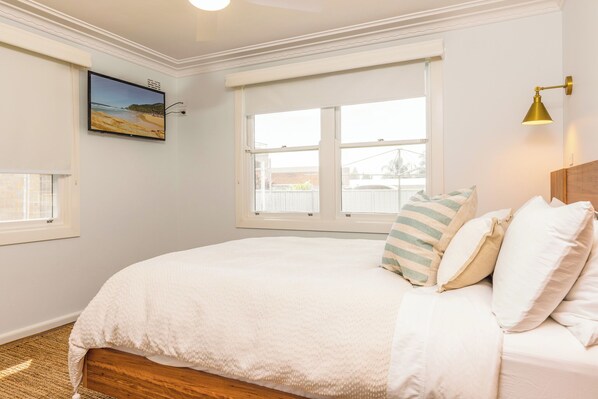Een slaapkamer met een groot bed, een raam met zonwering, een aan de muur bevestigde televisie en een bedlampje.