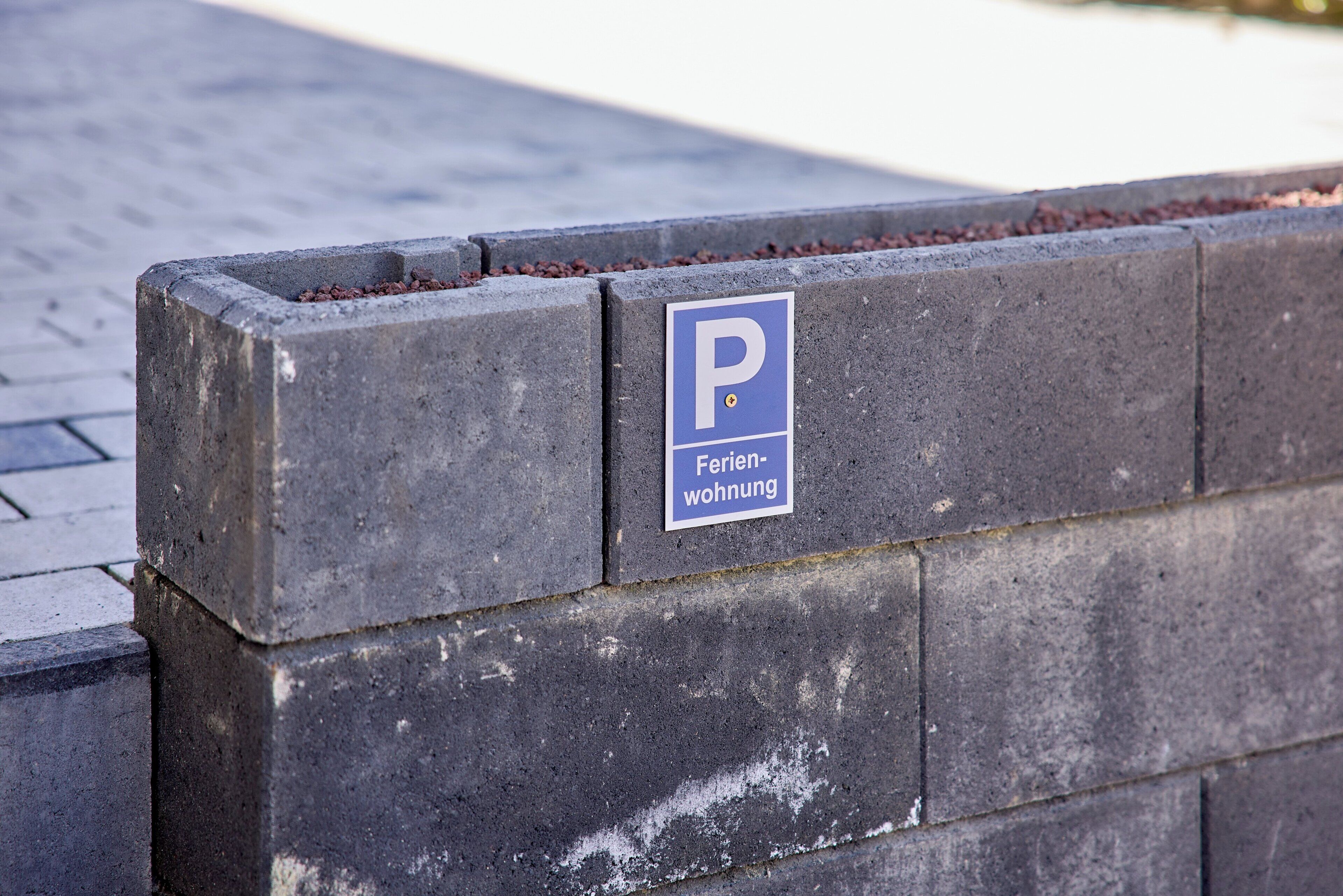 A parking sign with a blue background and white lettering, mounted on a concrete block.