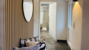 A hallway with a mirror, a door leading to a bathroom, and a wall-mounted light fixture.