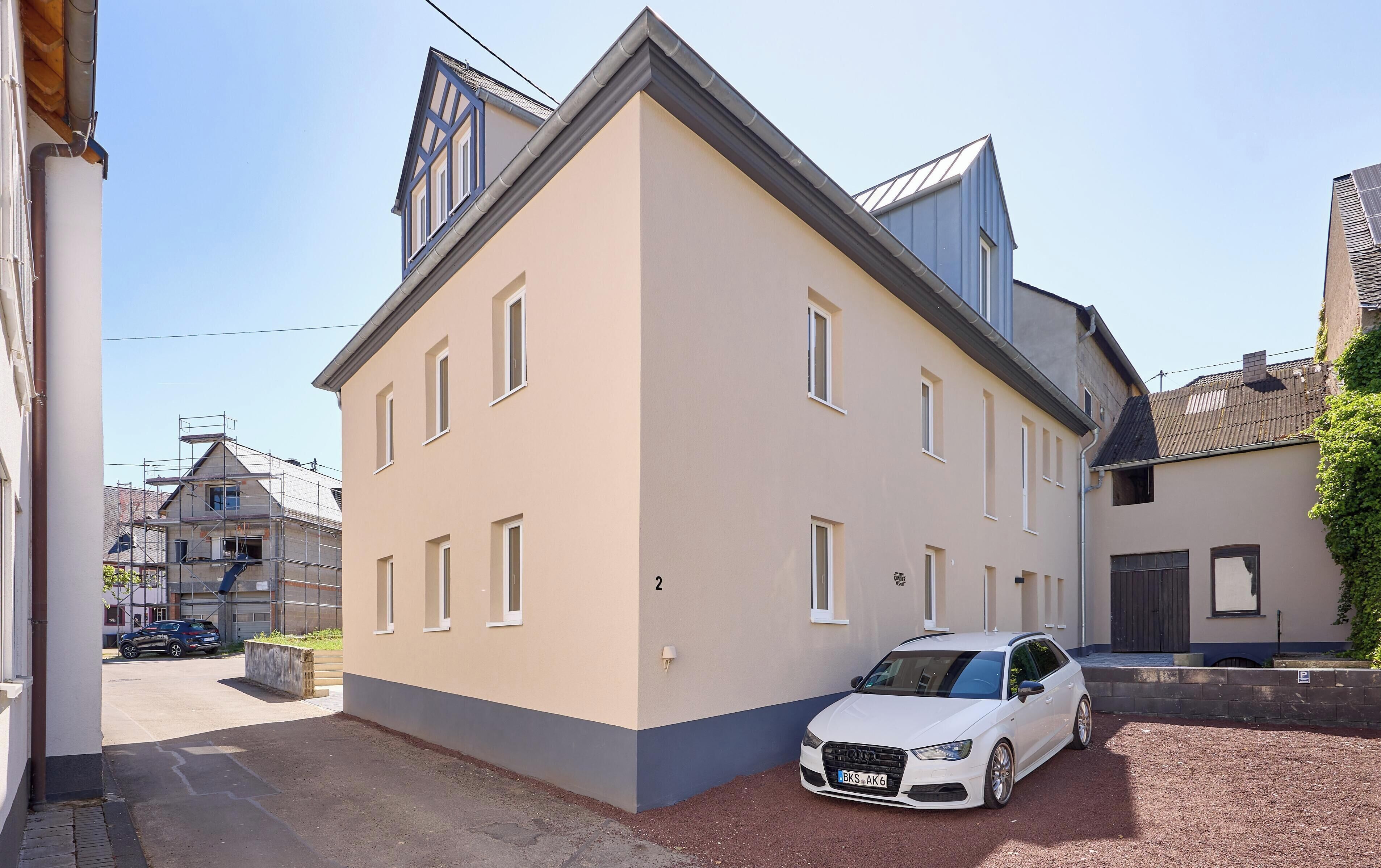 A two-story building with a beige facade, multiple windows, and a parked white car.