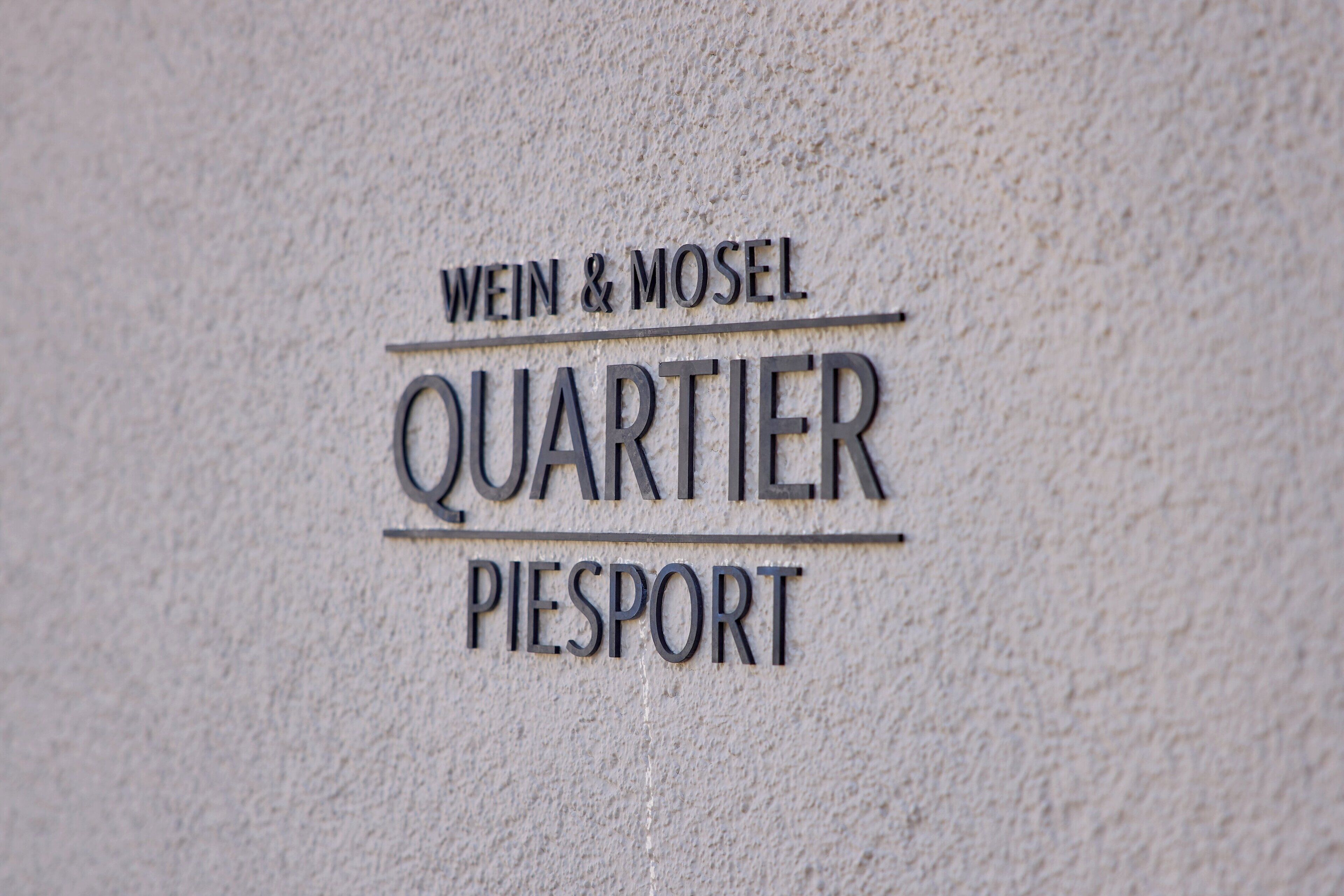 Una señal con la inscripción 'WEIN & MOSEL QUARTIER PIESPORT' grabado en una pared texturizada.