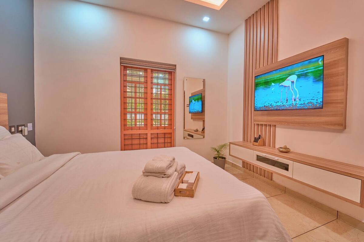 Une chambre d’hôtel moderne avec un grand lit, un téléviseur fixé au mur et une console en bois.
