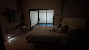 A dimly lit hotel room with a bed, a TV, a sliding door leading to a balcony, and a small table. - Sarang Resort Varkala by VOYE HOMES (Varkala)