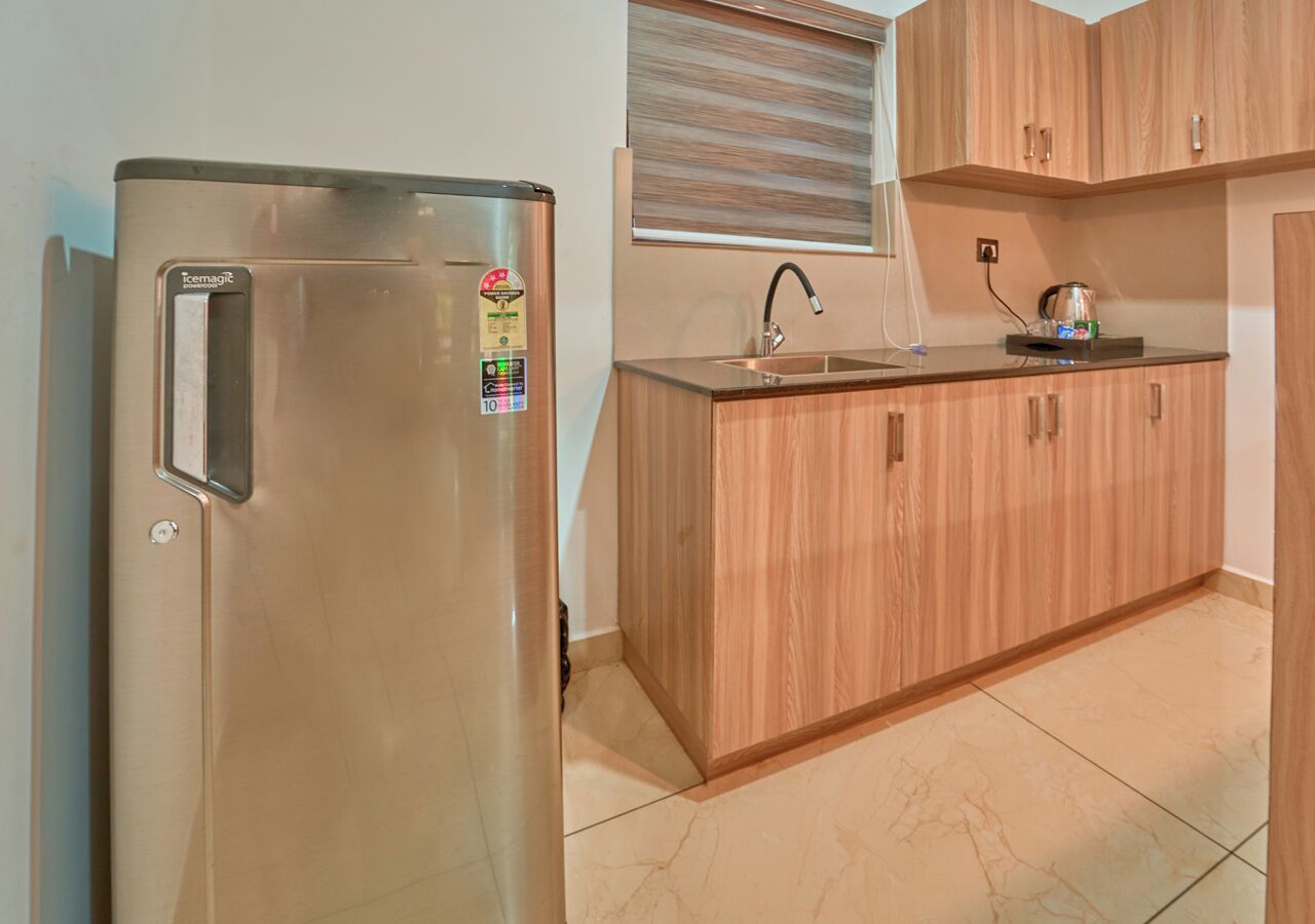 A kitchen with a stainless steel refrigerator, wooden cabinets, a sink, and a window with blinds.