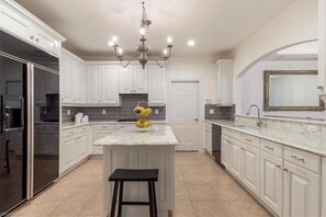 A modern kitchen with white cabinetry, a central island with a black stool, and a chandelier.