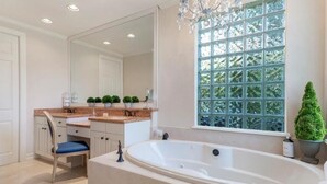 A bathroom with a large bathtub, a vanity with a mirror, and a window with a view of trees.