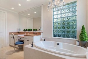 A bathroom with a large bathtub, a vanity with a mirror, and a window with a view of trees.