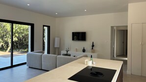 Ett modernt kök med en köksö i mitten, en platt-TV som är monterad på väggen och en stor skjutdörr i glas som leder ut till ett utomhusområde.