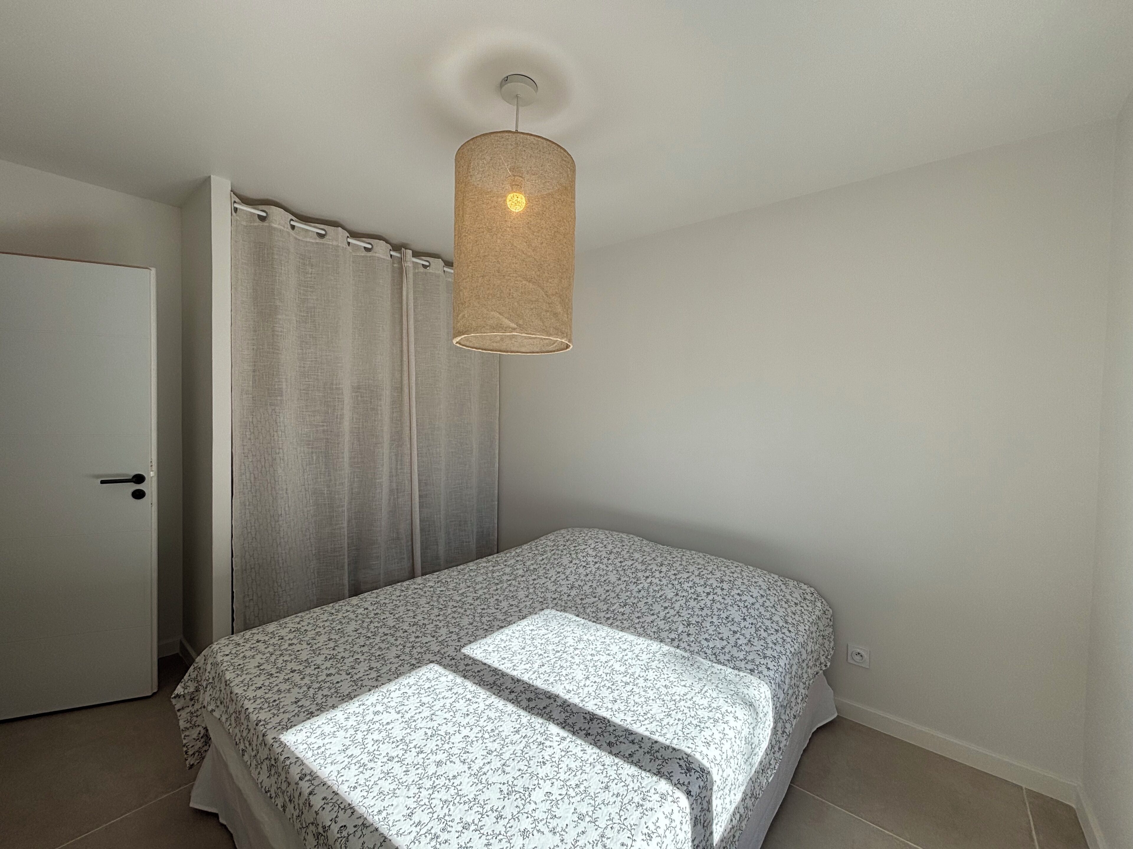 A bedroom with a bed, a door, and a hanging light fixture.