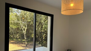 Ett sovrum med en stor skjutdörr i glas som leder ut till ett utomhusområde, en säng med en vit madrass och en hängande lampa.