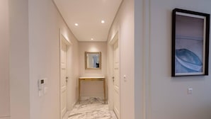 A hallway with a marble floor, a gold-framed mirror, and a framed artwork on the wall.