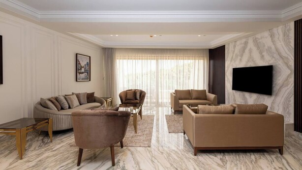 A spacious living room with a marble floor, a sofa set, a coffee table, and a flat-screen TV mounted on the wall.