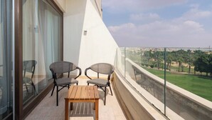 A balcony with two chairs and a small table, offering a view of a golf course and cityscape.