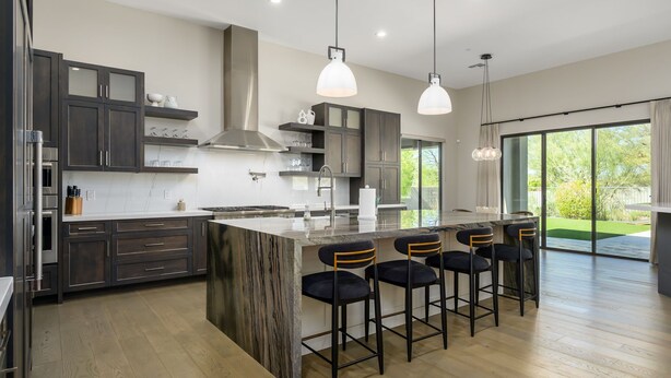 A modern kitchen with dark cabinets, a central island, bar stools, and pendant lighting. - Luxury in North Scottsdale sleeps 10 (Scottsdale)