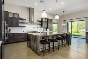 A modern kitchen with dark cabinets, a central island, bar stools, and pendant lighting.