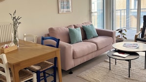 A living room with a sofa, a coffee table, a dining table with chairs, a vase with flowers, and a framed picture on the wall.