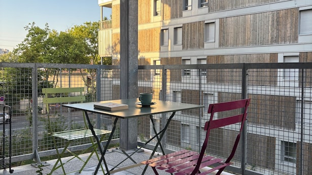 A balcony with a table and chairs, potted plants, and a view of a modern building.