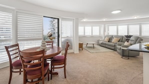 A modern living room with a dining area, featuring a round table, wooden chairs, a sofa, and a coffee table.