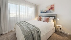 A neatly arranged bedroom with a large bed, a bedside table with a lamp, and a painting on the wall.