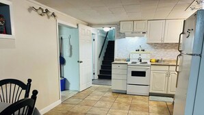 A compact kitchen with white cabinets, a stove, and a refrigerator. A dining table with a chair is visible in the foreground. - 1 bedroom apartment, centrally located and newly renovated (Moncton)