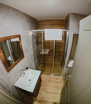 A bathroom with a glass-enclosed shower, a sink with toiletries, and a mirror.