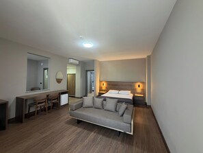 A modern hotel room with a bed, a sofa, a desk, and a mirror.