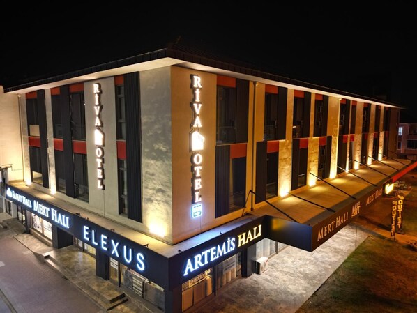 A modern hotel with a prominent 'RIVA HOTEL' sign, multiple entrances, and a covered outdoor area.